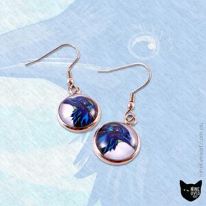 Blue Raven earrings on faint background featuring original artwork